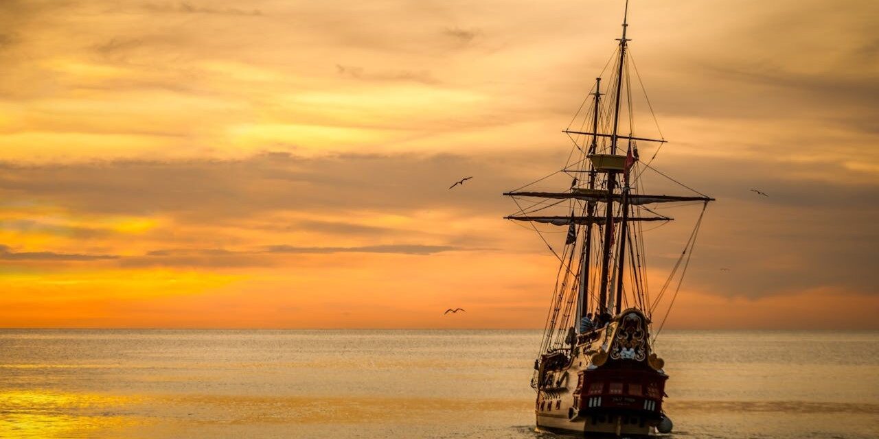 Zeilschip bij zonsondergang Historisch zeilschip vaart bij zonsondergang op kalme zee, gerelateerd aan bakboord en stuurboord