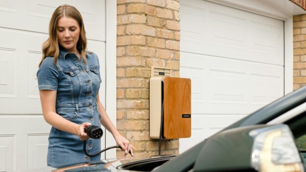 Vrouw sluit elektrische auto aan op slimme laadpaal thuis, geschikt voor vehicle-to-grid toepassingen.