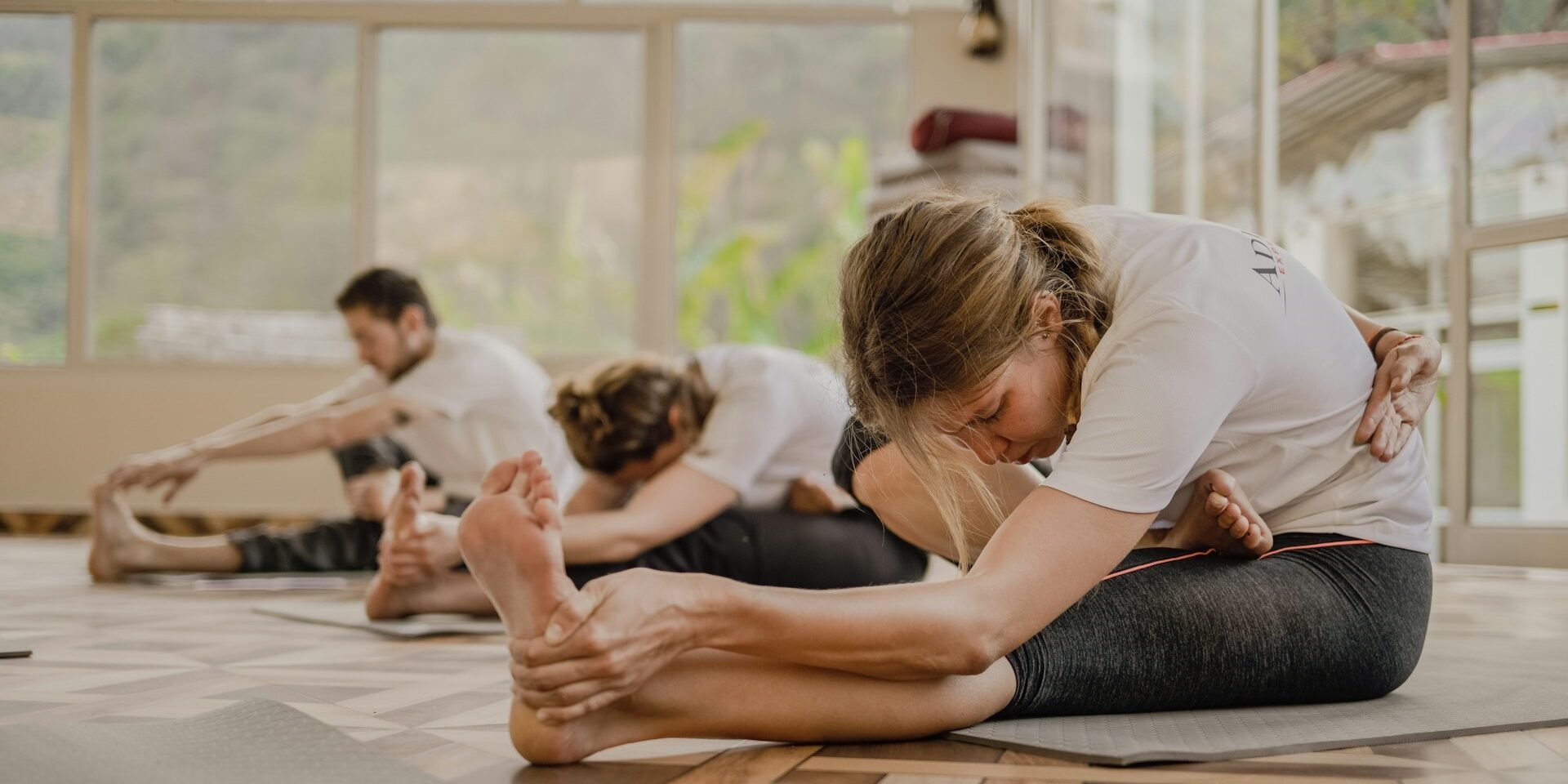 Matpilates groepsles voorwaartse stretch Groep mensen doet voorwaartse stretch tijdens matpilates in een zonnige studio