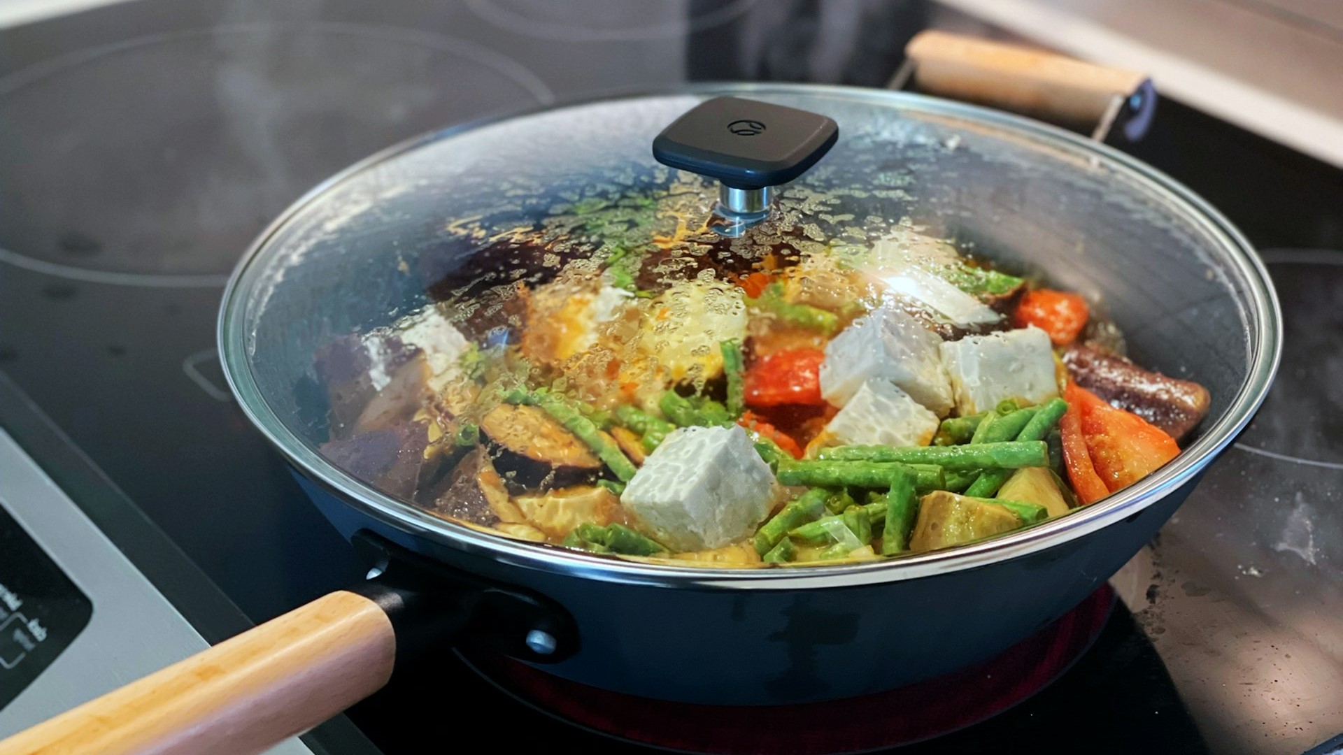 Groentemix met tofu suddert in een pan met glazen deksel op een inductiekookplaat tijdens het inductie