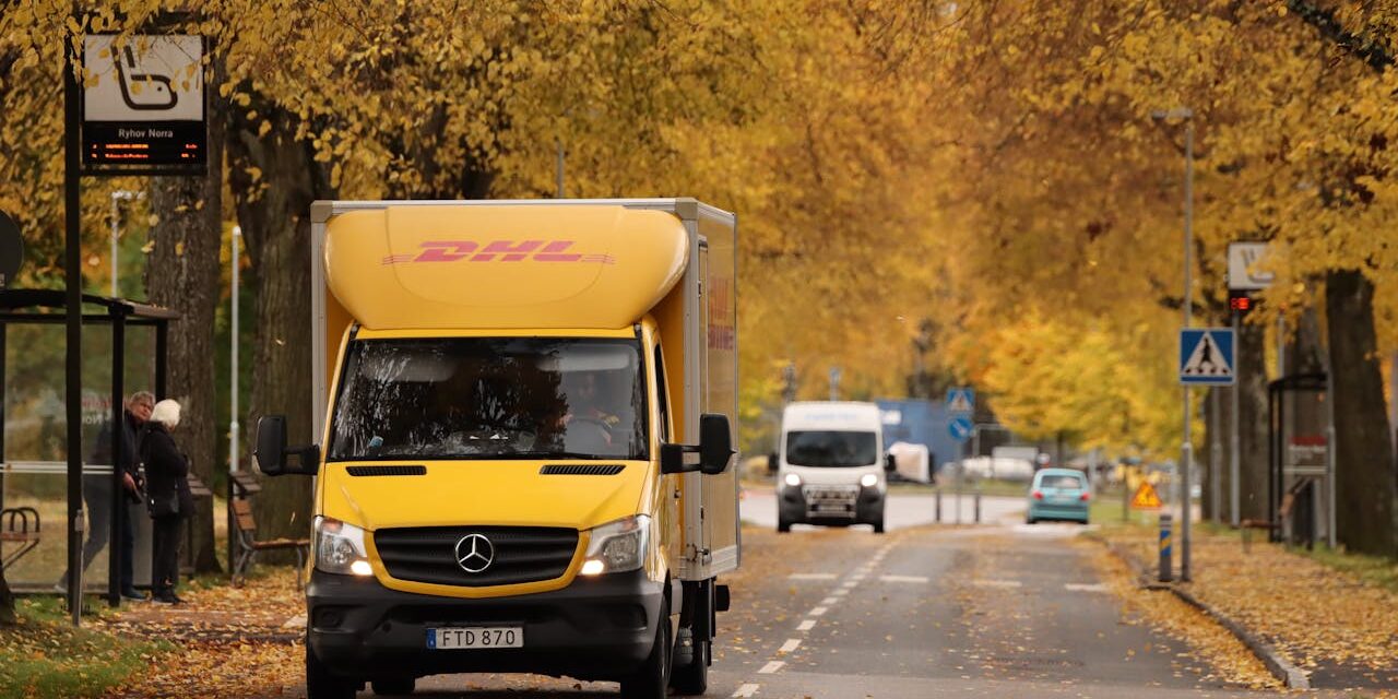 DHL-busje rijdt door een herfstlandschap als onderdeel van same day delivery in de stad.