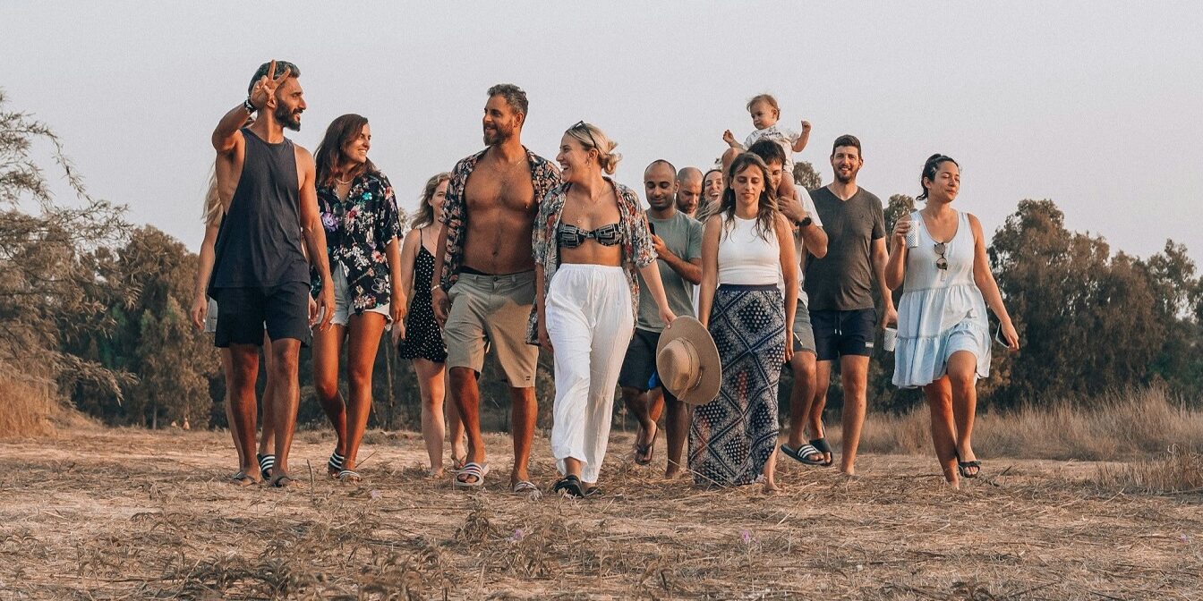 Groep vrienden wandelt ontspannen over een droog grasveld, de entourage straalt warmte en saamhorigheid uit.