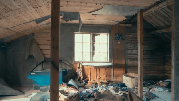 Vervallen zolderkamer vol puin en afbladderend hout, die de vergankelijkheid en decadentie van een oude woning toont