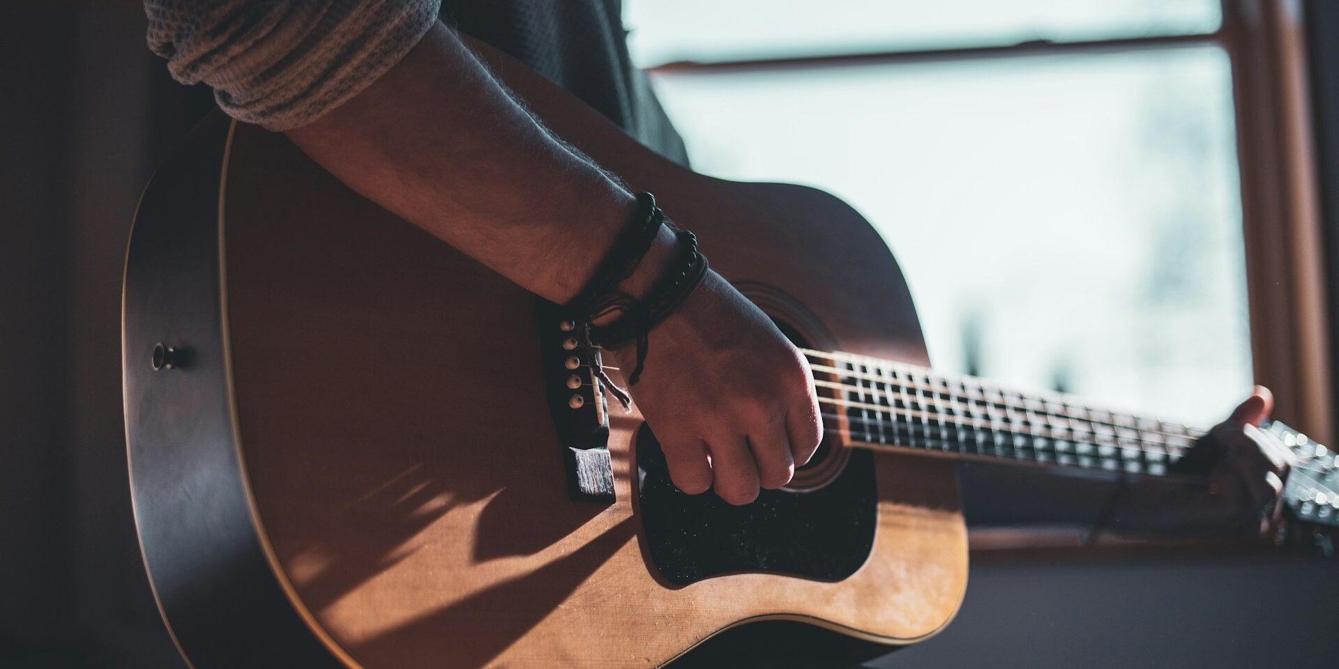 Persoon speelt akoestische gitaar bij raamlicht, waarbij mensuur gitaar invloed heeft op speelgevoel