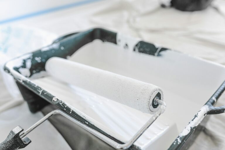 Verfroller met witte verf in verfbak tijdens schilderen voor een gelijkmatige dekking van de muur