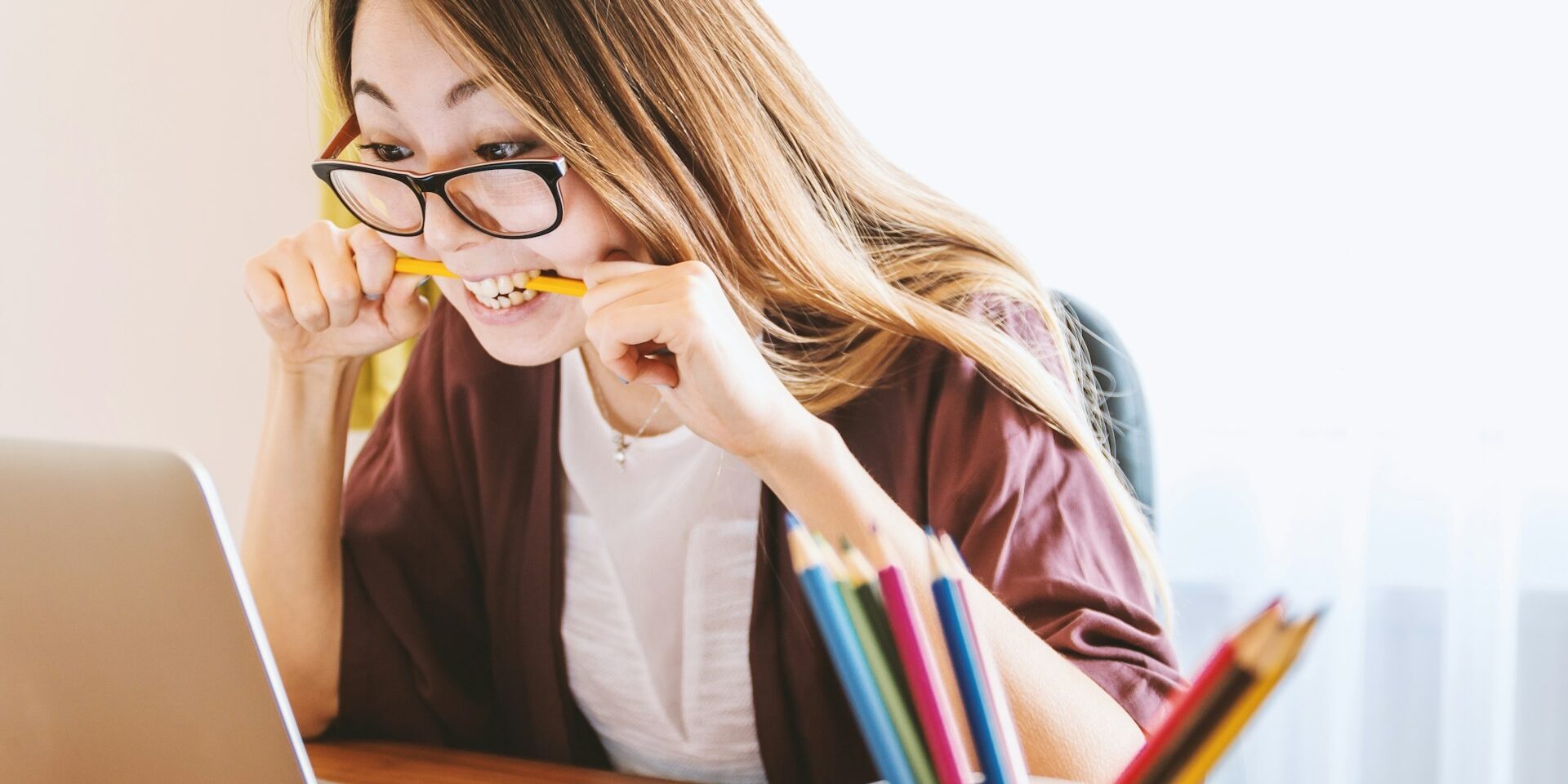 Vrouw bijt op potlood terwijl ze gespannen naar laptop kijkt door prestatiedruk tijdens studie