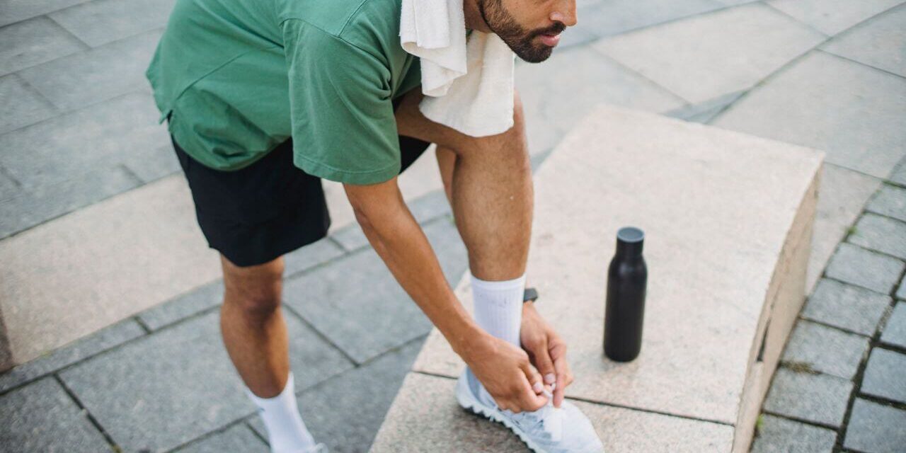 Man aan het rennen Hardloper strikt zijn schoenen voor een training waarbij stack height invloed heeft op comfort en demping